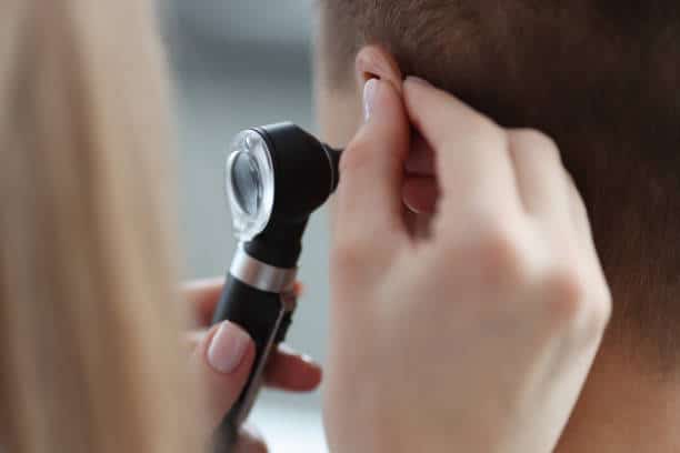 Otorhinolaryngologist pulling ear with his hand and looking at it with otoscope closeup. Otoscopy concept